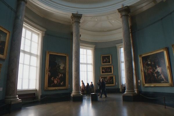 A long gallery corridor with arched doorways and rows of large classical paintings under soft natural light